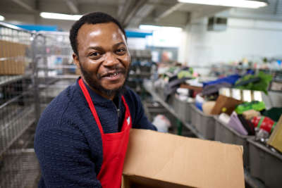 thrift store employee smiles as he carries a box of donations to the retail floor